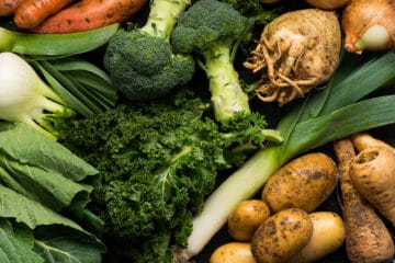 An assortment of fresh vegetables including kale, broccoli, celeriac, potatoes, parsnips, fennel, onions, and sweet potatoes.