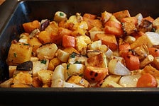 Roasted root vegetables seasoned with cardamom in a black roasting pan.
