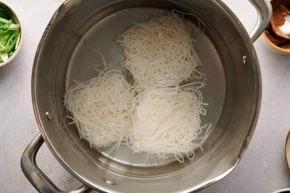 Rice noodles boiling in a pot.